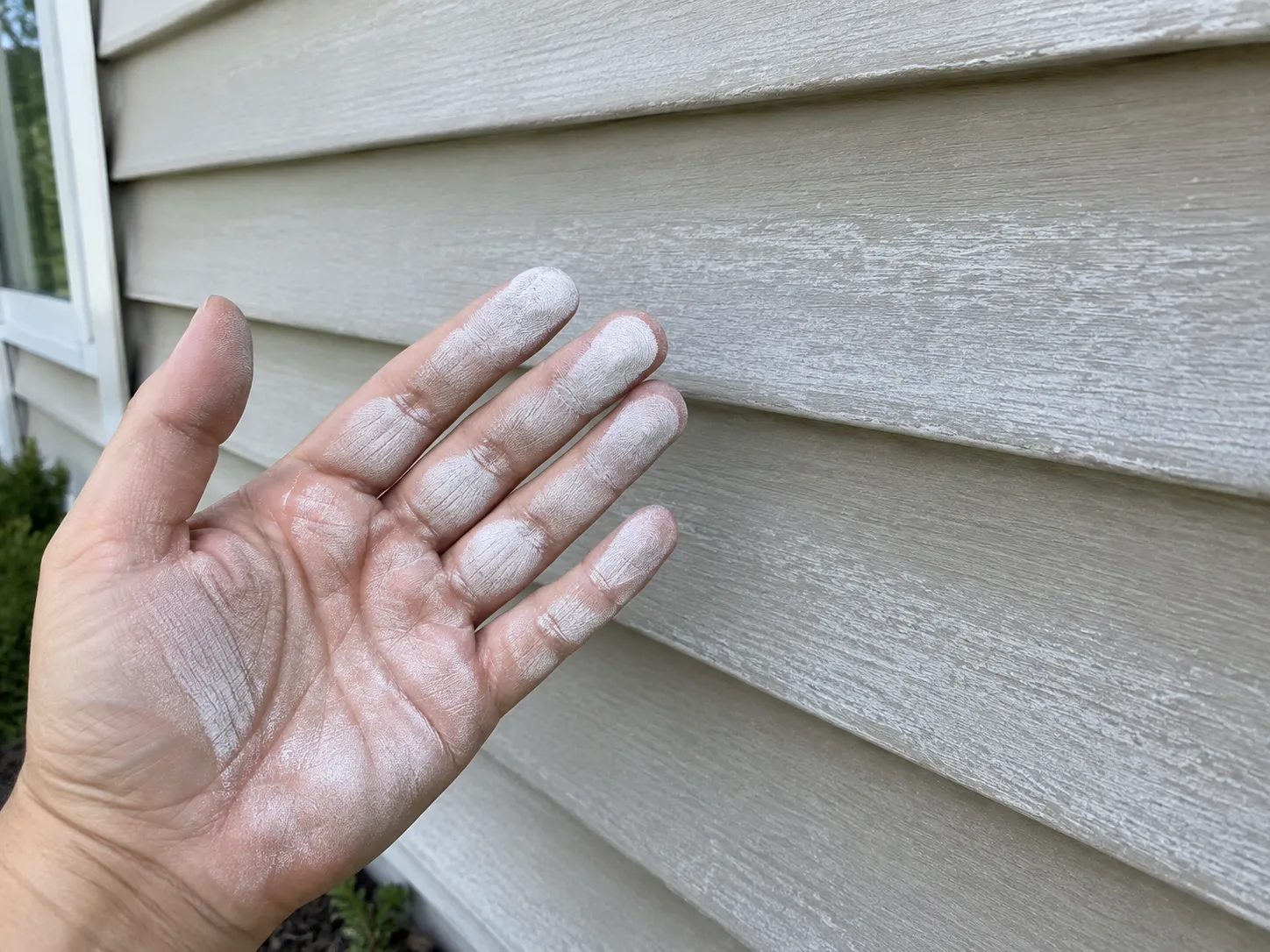 Chalk test on vinyl siding showing white oxidation residue on a hand